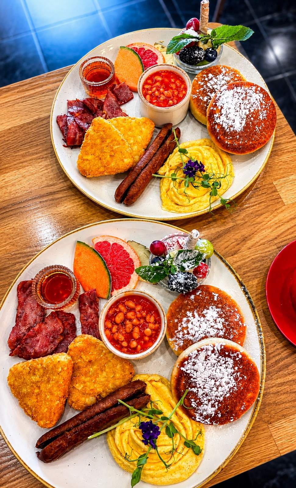 Two generous breakfast plates with eggs, sucuk, fruit and fresh sides